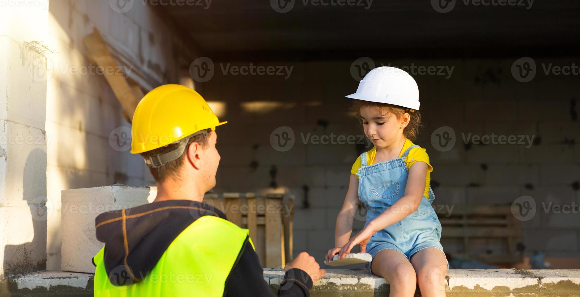 Dad and daughter are at construction site of their future home. The choice of the future profession of a builder is inherited by child. The expectation of moving, the dream of a house. Mortgage, loan photo