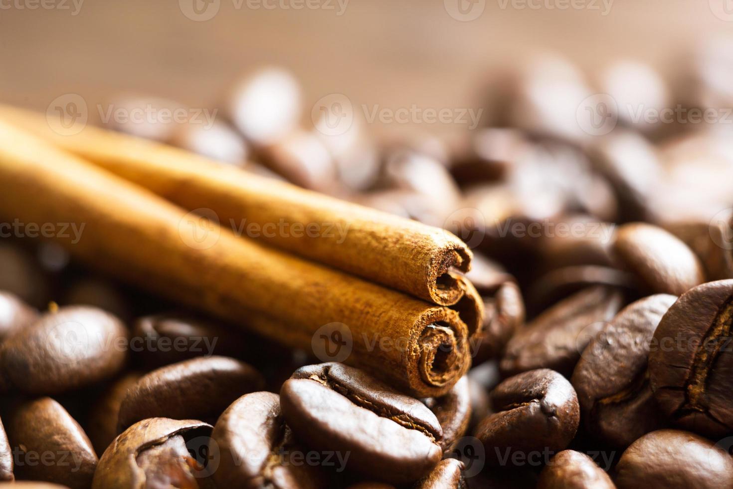 A stick of cinnamon lies on the roasted coffee beans close-up - fragrant macro backgrounds. Brown arabica coffee beans are scattered on the wooden table. Copy space photo