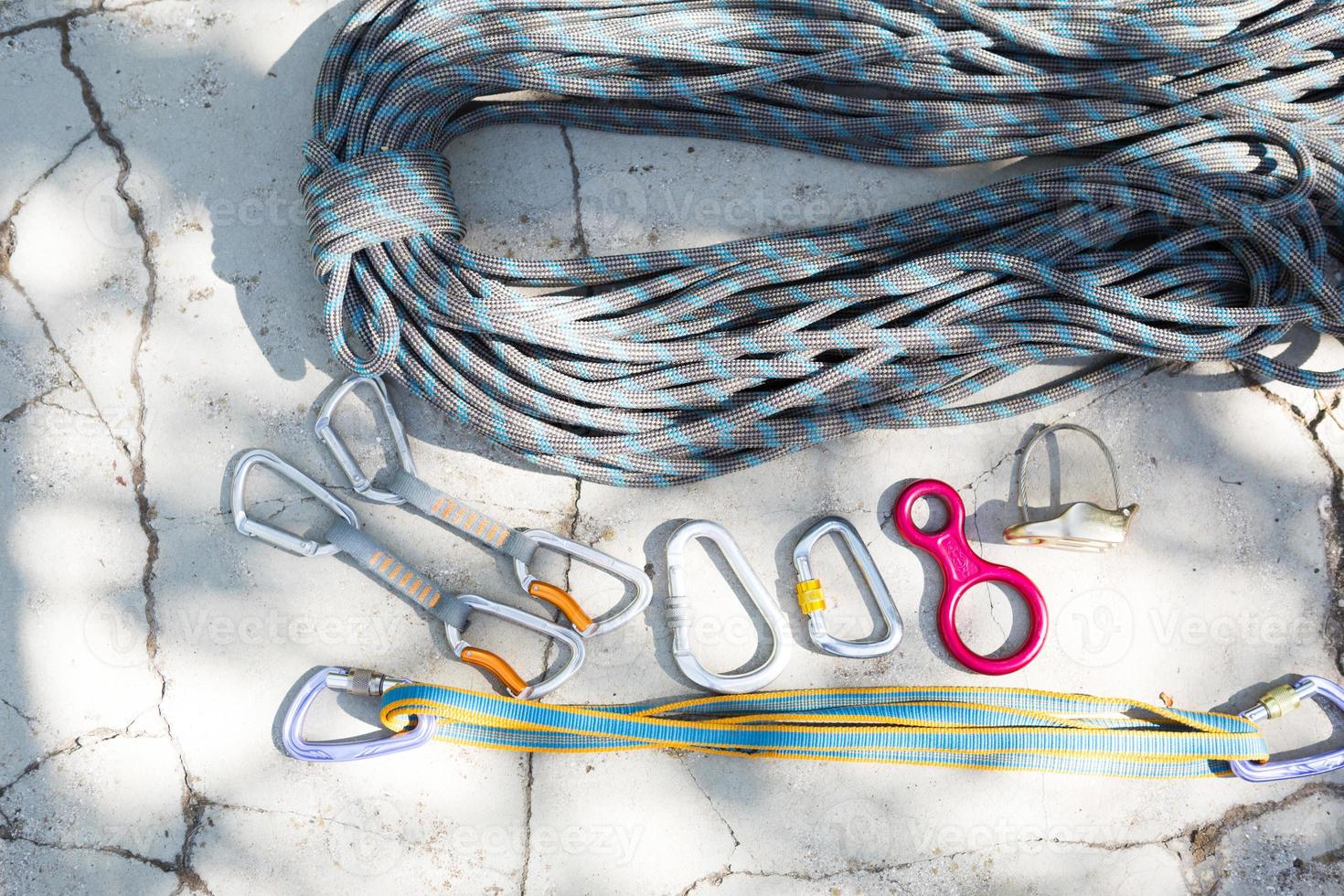 Coiled climbing rope and steel carabiner. Mountain climbing equipment harness, brakes, quickdraws, self-insurance, belay device eight. On a stone background with cracks. Flatlay, copy space photo