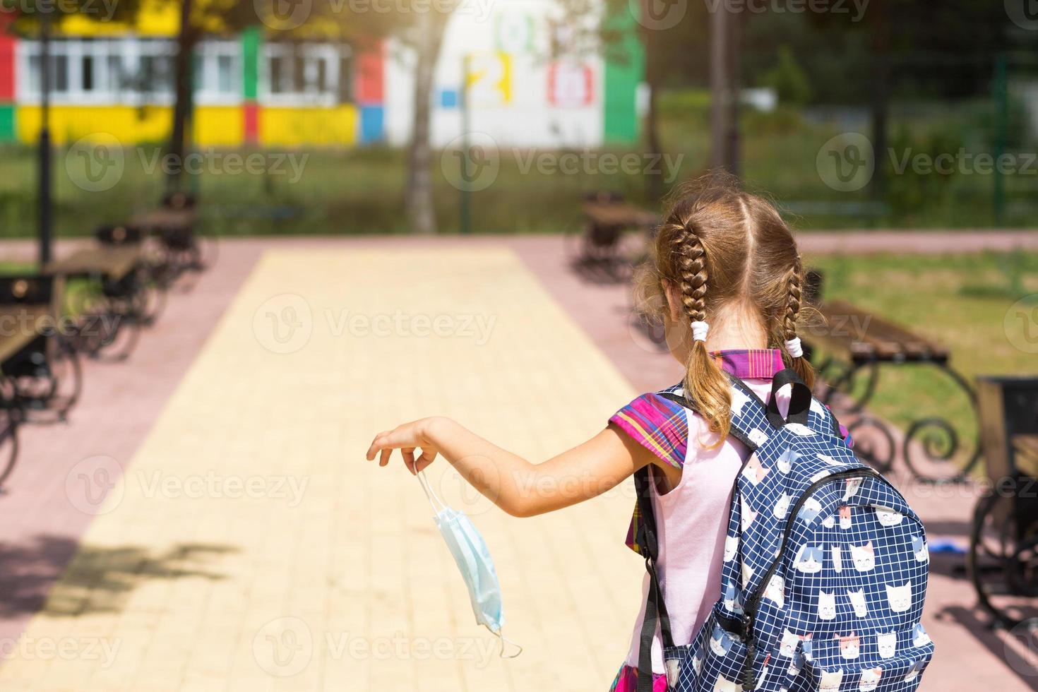 Girl with a backpack near the school after classes with the medical mask removed, unhappy, tired. Coronavirus infection, security measures, precaution. photo