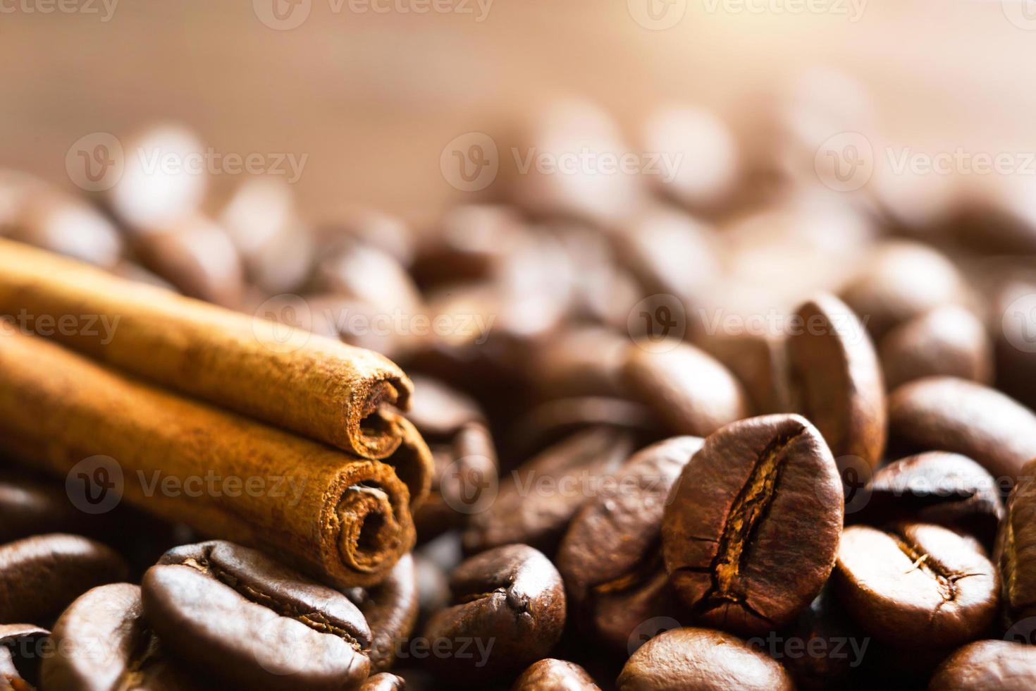 A stick of cinnamon lies on the roasted coffee beans close-up - fragrant macro backgrounds. Brown arabica coffee beans are scattered on the wooden table. Copy space photo