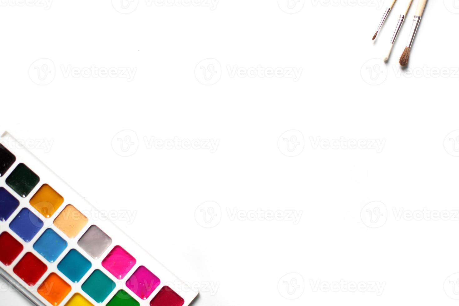 A palette of eighteen-color watercolors and paintbrushes on a white background with space for text. photo