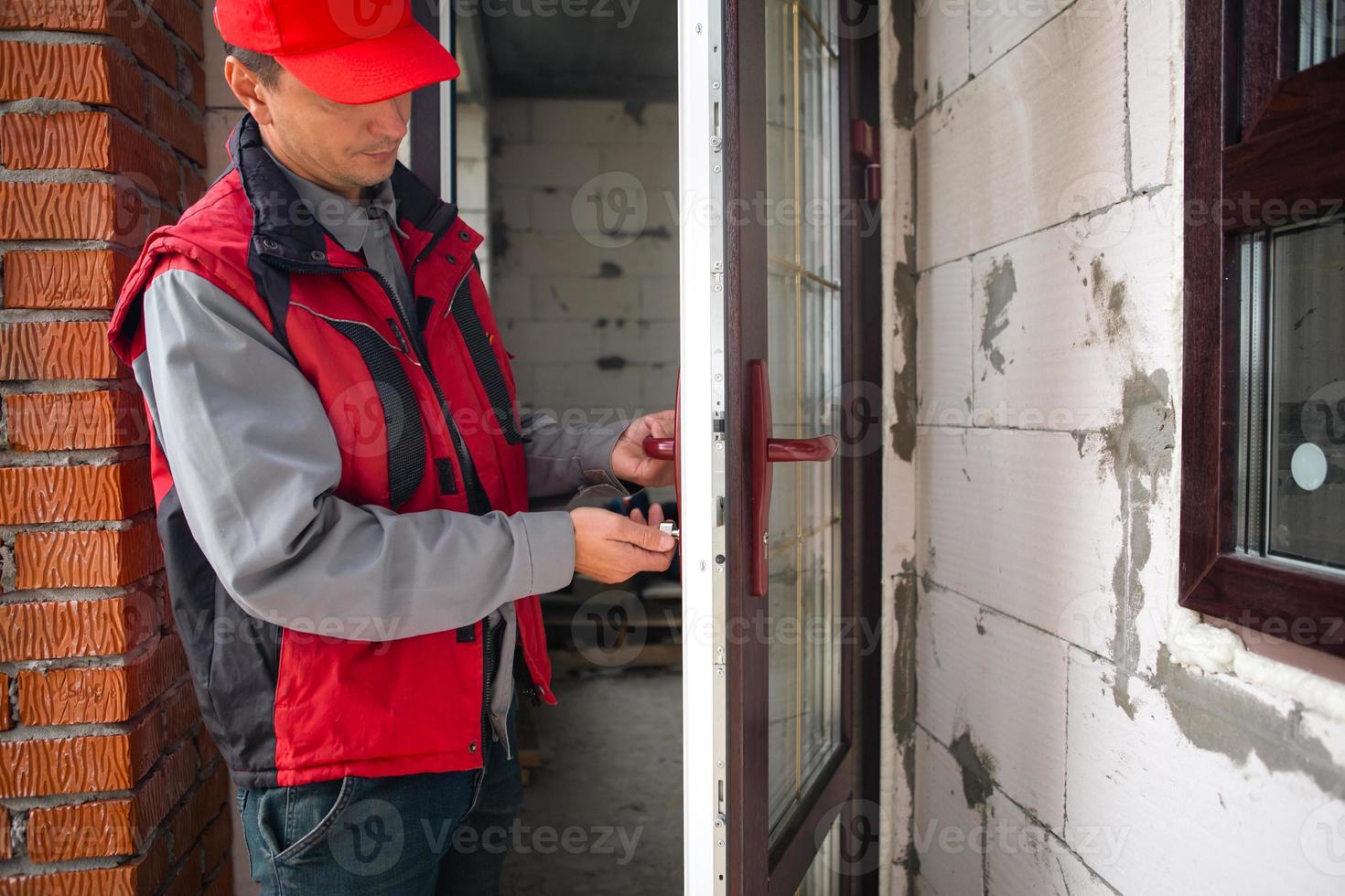 Master sets up a door handle with multi-lock plastic door with wood lamination and gold layout in private house. Installation of windows and doors, glazing of the cottage, replacement of the mechanism photo