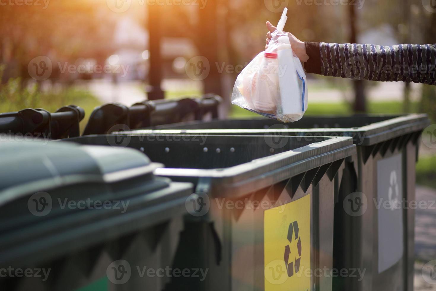 Hand with a bag of plastic garbage over containers for separation and sorting in Russia with the words Glass, plastic, household waste. photo