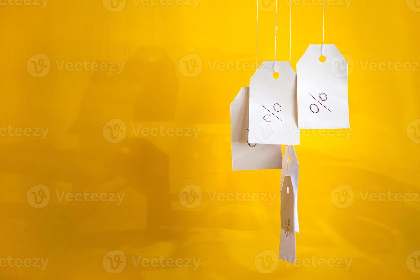 White tags with the percent sign hang on strings on a yellow background with shadows. Commerce, discount, sale, trade offer. Copy space, mock up. photo