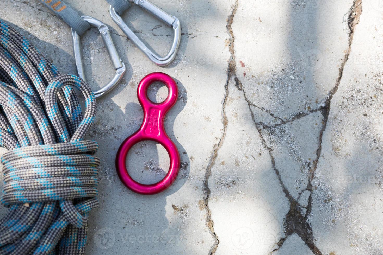 Coiled climbing rope and steel carabiner. Mountain climbing equipment harness, brakes, quickdraws, self-insurance, belay device eight. On a stone background with cracks. Flatlay, copy space photo