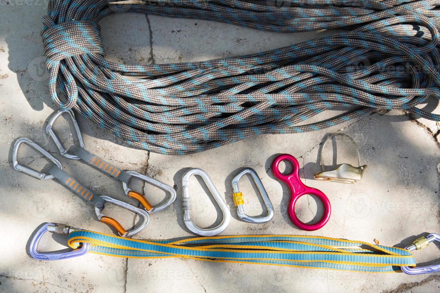 Coiled climbing rope and steel carabiner. Mountain climbing equipment harness, brakes, quickdraws, self-insurance, belay device eight. On a stone background with cracks. Flatlay, copy space photo