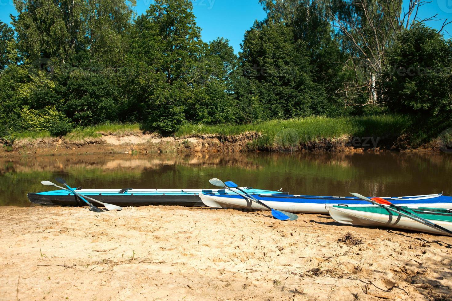 Tourist canoes with paddles stand on the river coast in summer on a water hike. Rafting on inflatable and frame double and triple kayak boats, family trip, extreme adventure in summer photo