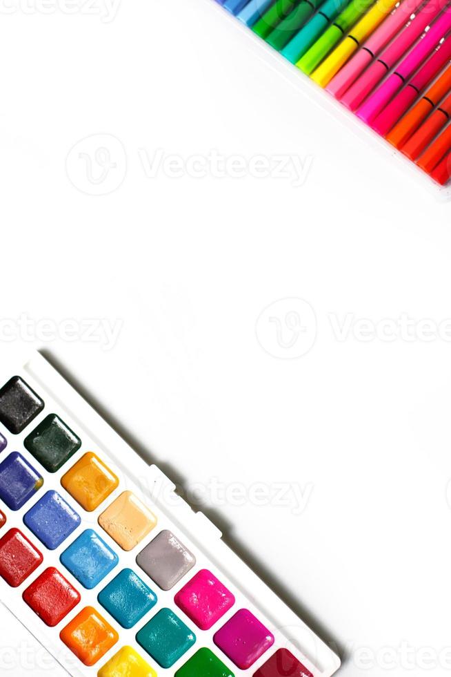 una paleta de acuarelas de color con pinceles y marcadores sobre un fondo blanco con espacio para texto. foto