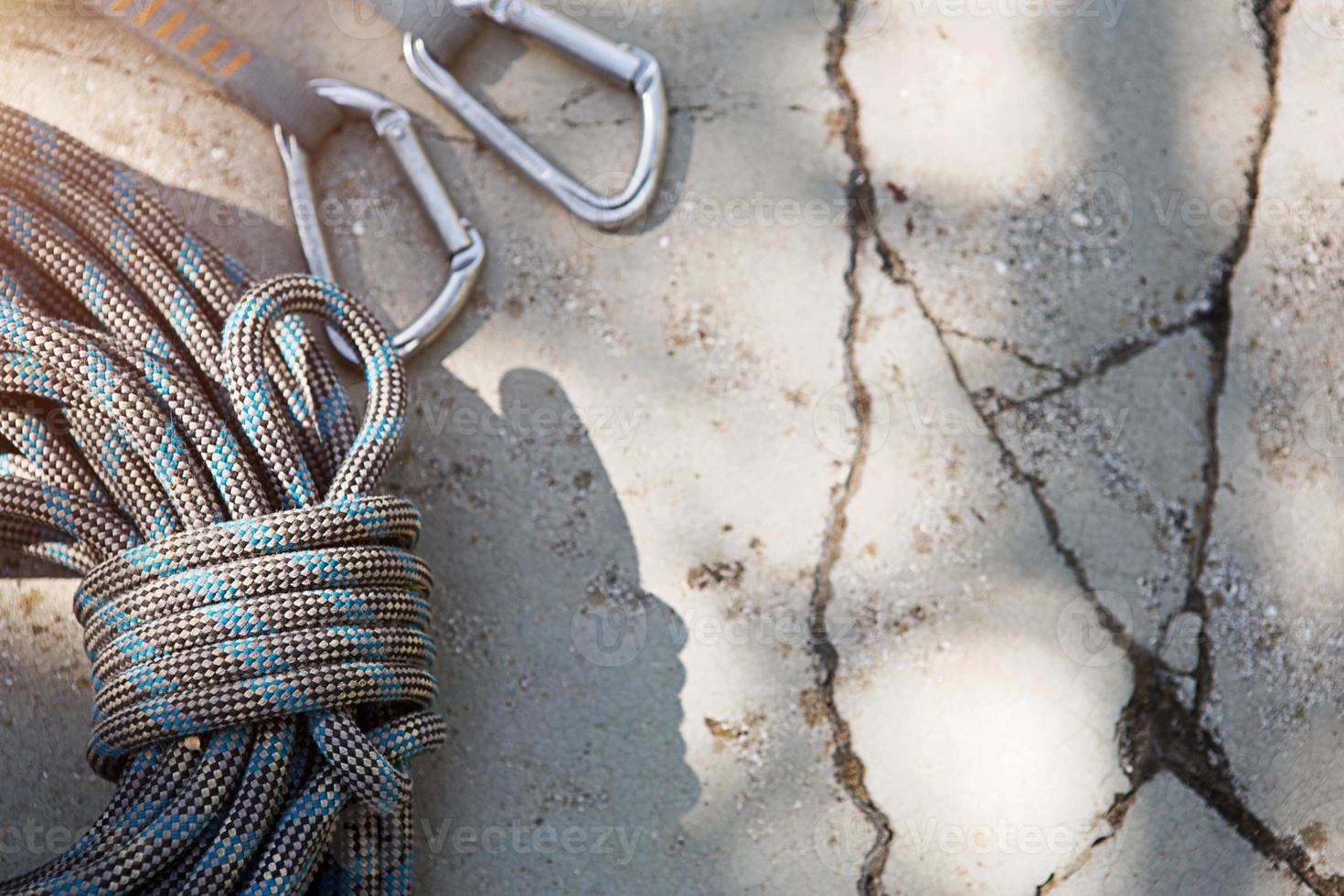 Coiled climbing rope and steel carabiner. Mountain climbing equipment harness, brakes, quickdraws, self-insurance, belay device eight. On a stone background with cracks. Flatlay, copy space photo