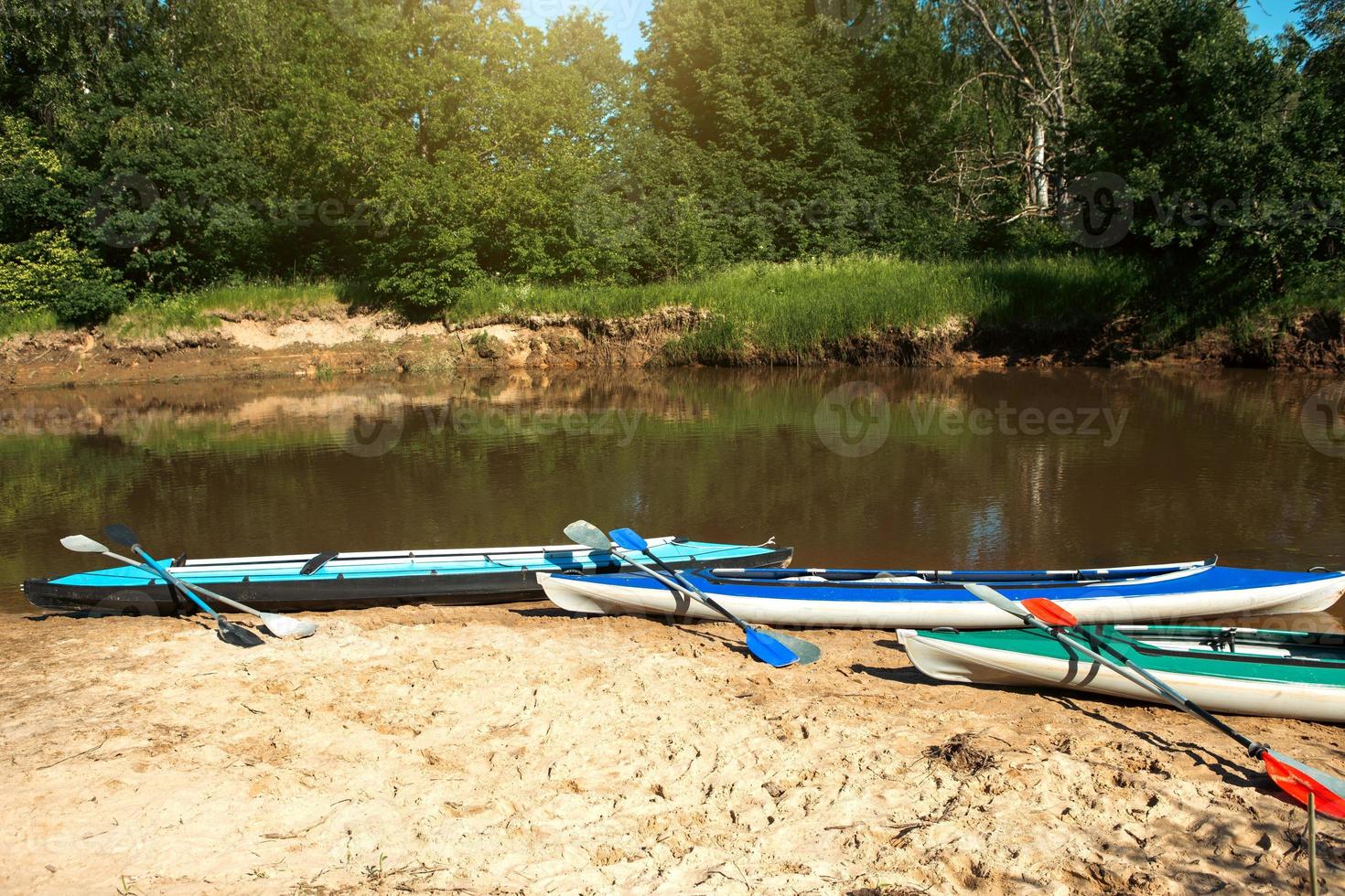 Tourist canoes with paddles stand on the river coast in summer on a water hike. Rafting on inflatable and frame double and triple kayak boats, family trip, extreme adventure in summer photo