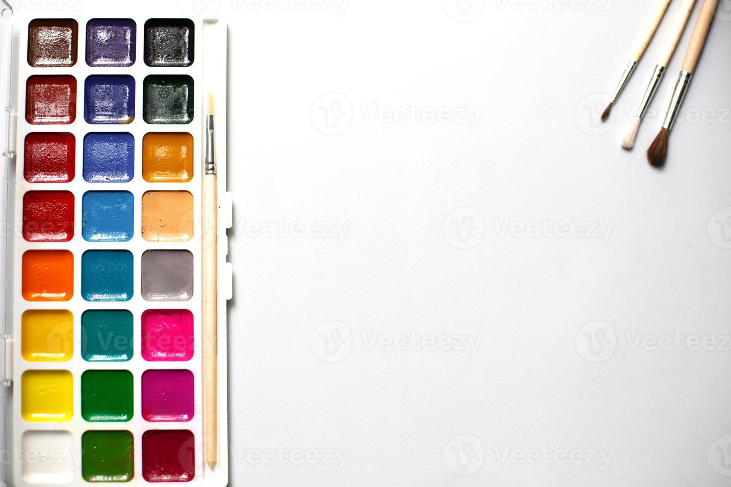 A palette of eighteen-color watercolors and paintbrushes on a white background with space for text. photo