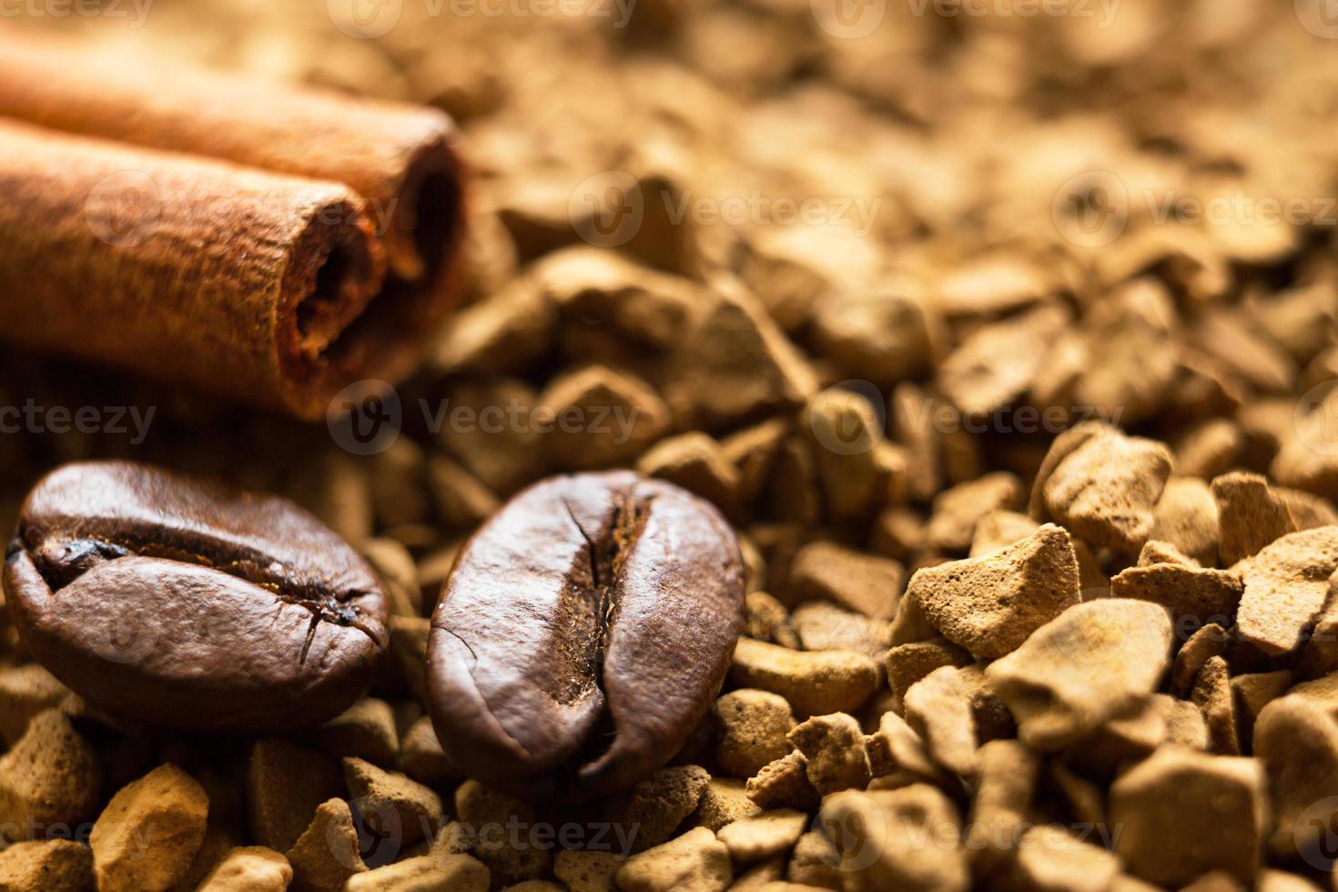 Beans of natural roasted coffee and a cinnamon stick close-up lie on the granules of instant coffee. Ingredients of a fragrant invigorating drink, macro background. Copy space photo