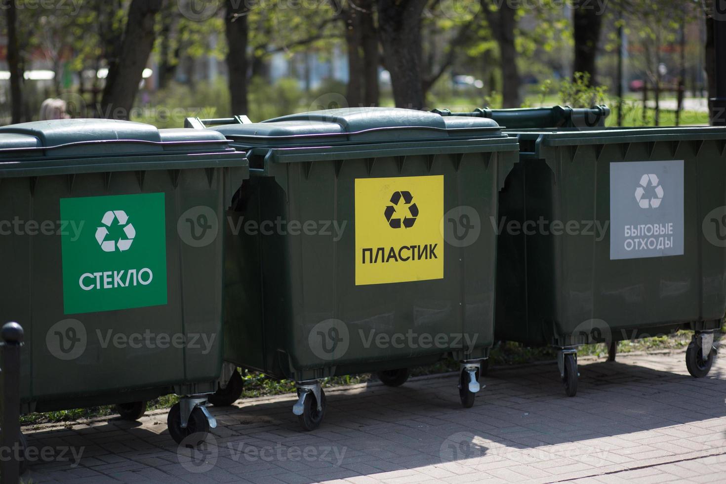 Hand with a bag of plastic garbage over containers for separation and sorting in Russia with the words Glass, plastic, household waste. photo