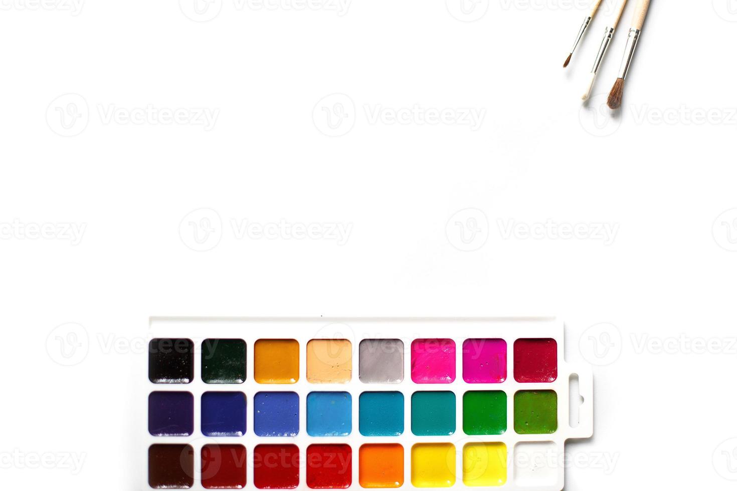 A palette of eighteen-color watercolors and paintbrushes on a white background with space for text. photo