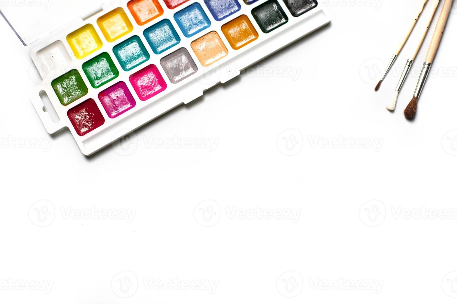 A palette of eighteen-color watercolors and paintbrushes on a white background with space for text. photo