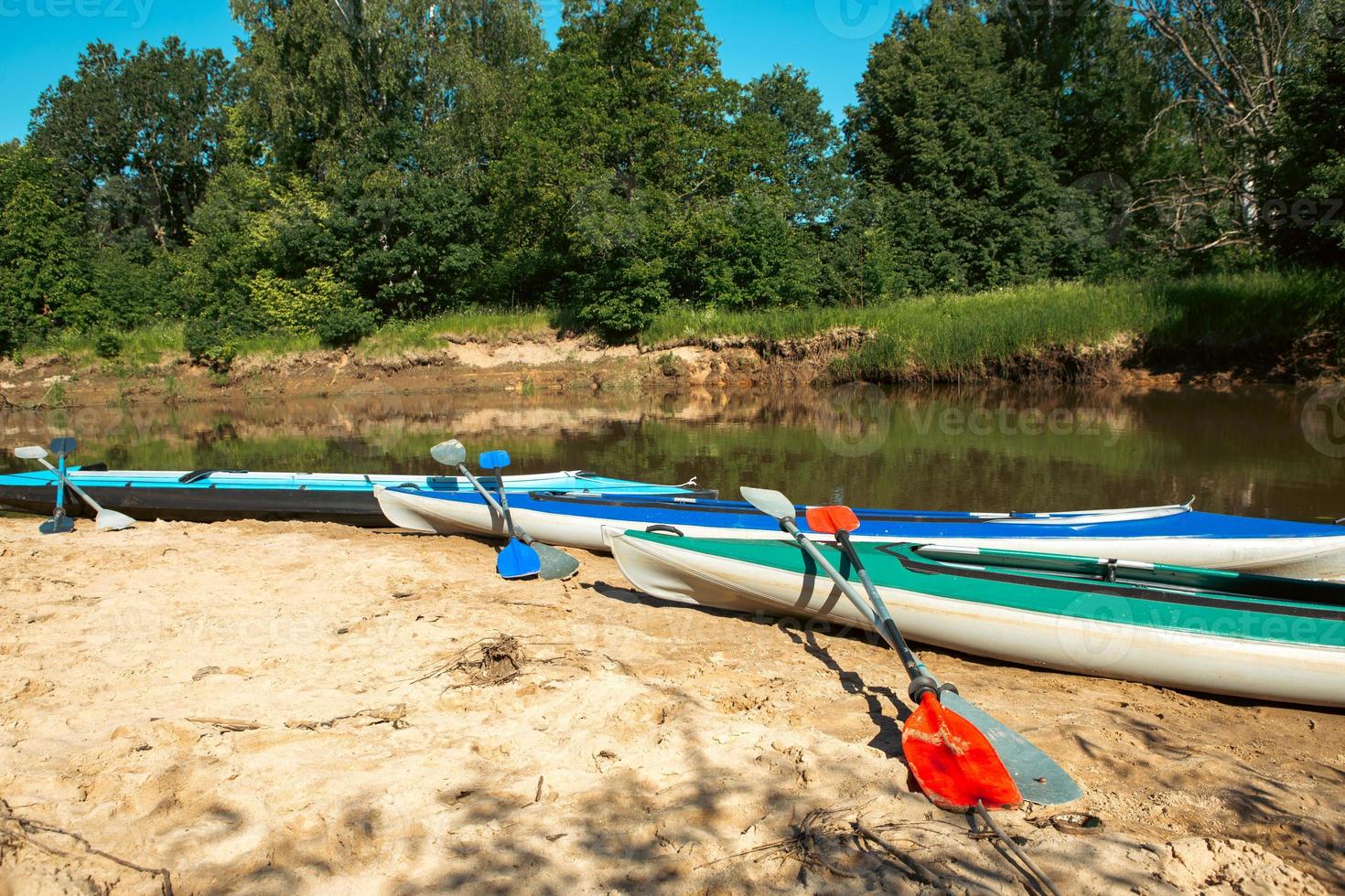 Tourist canoes with paddles stand on the river coast in summer on a water hike. Rafting on inflatable and frame double and triple kayak boats, family trip, extreme adventure in summer photo