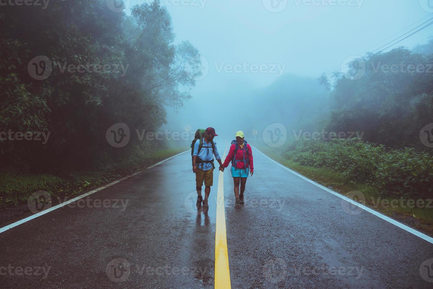 Lover asian man and asian women travel nature. Walk on the road route. traveling nature happily. Amid the mist rainy. photo