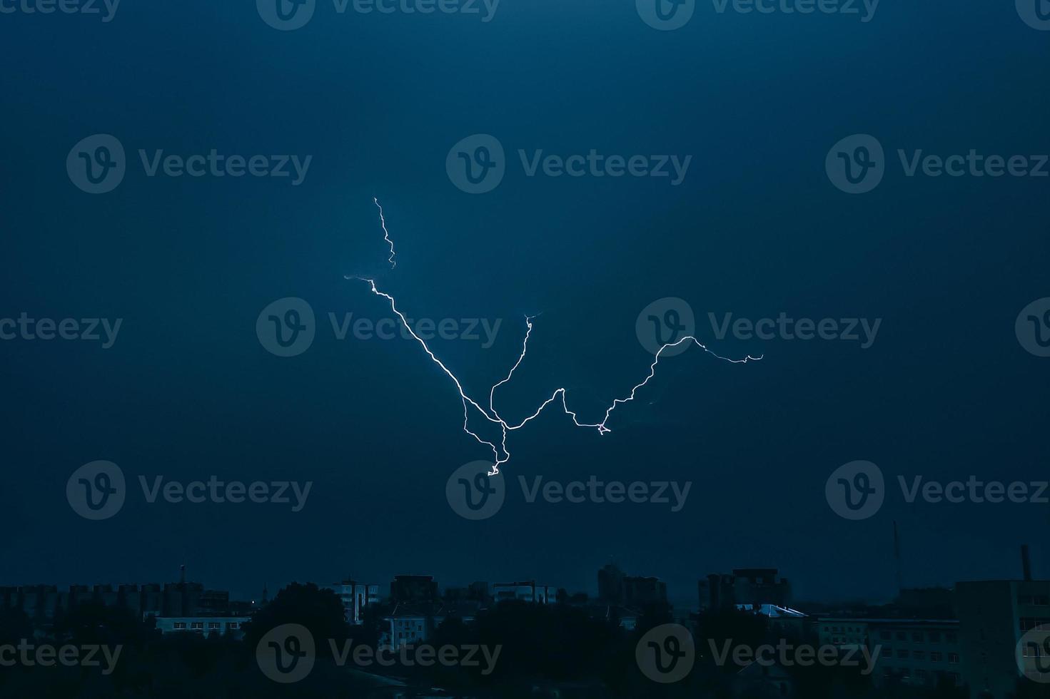 Lightning in sky over city. Bright flashes on dark night. Thunderclouds and electricity discharges in  atmosphere. photo