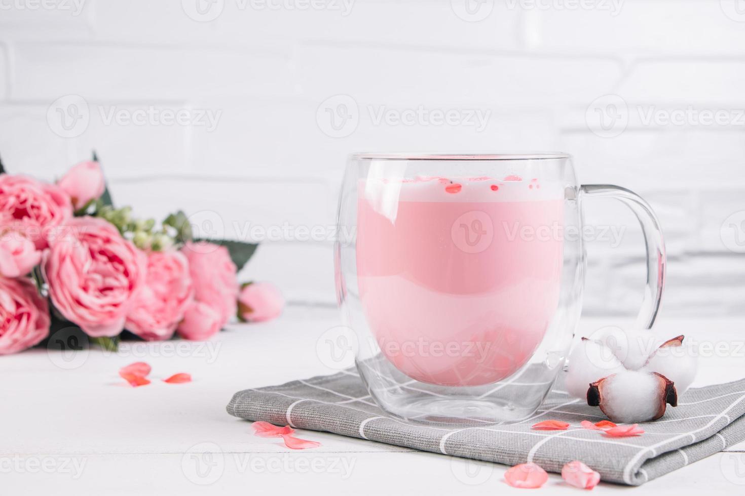 Moon milk. Pink matcha with rose petals. Transparent cup with trendy vegan whipped tea on white background. Relaxing drink for sleepy time. photo