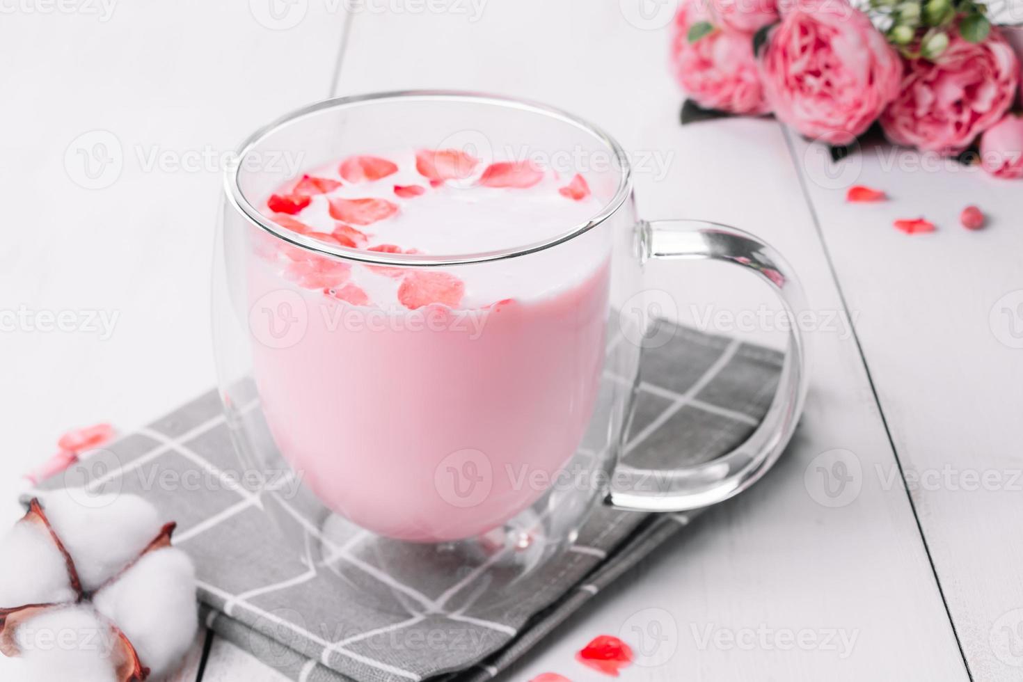 Moon milk. Pink matcha with rose petals. Transparent cup with trendy vegan whipped tea on white background. Relaxing drink for sleepy time. photo