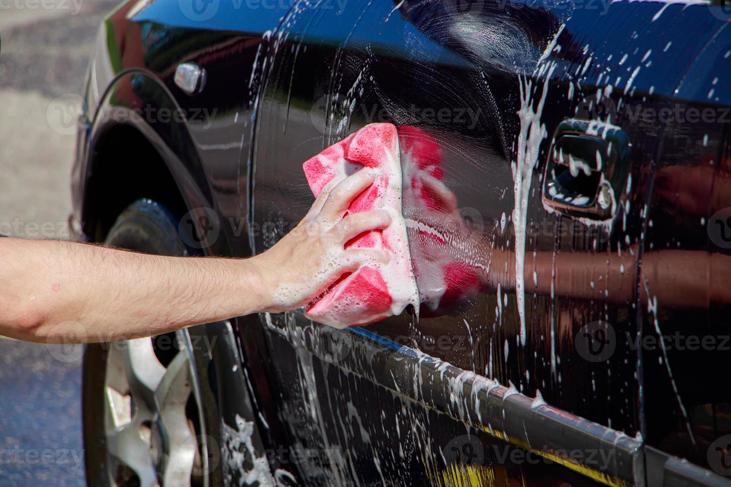 Man washes car wheel. Male hand holds pink sponge with soapy foam for cleaning. photo
