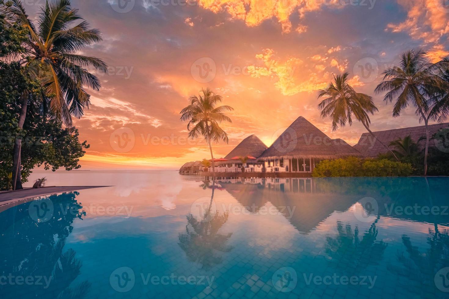 Outdoor tourism landscape. Luxury beach resort, infinity swimming pool and beach chairs loungers umbrellas with palm trees and sunset sea sky reflection. Summer island relax travel idyllic vacation photo
