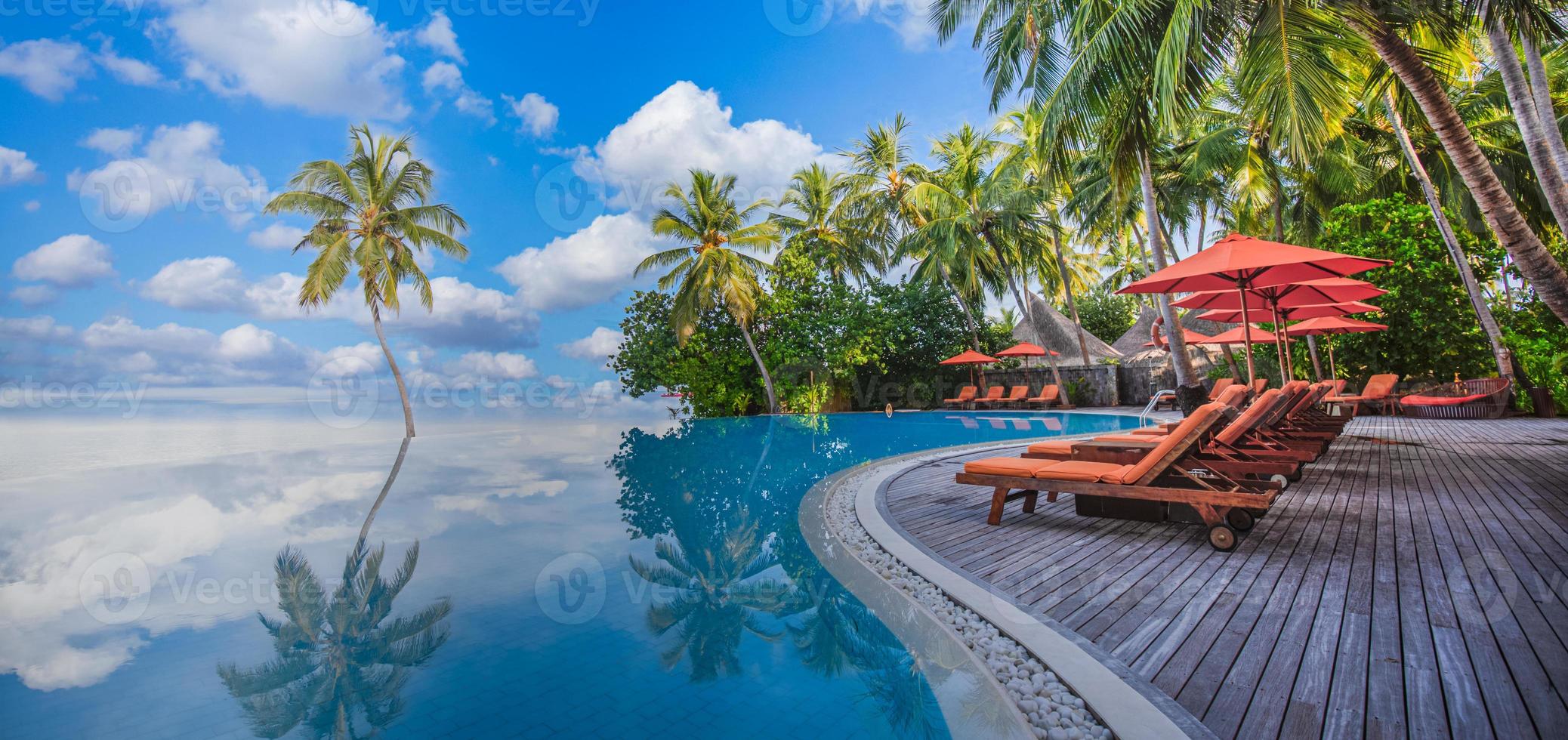 Panoramic holiday landscape. Luxurious beach resort hotel swimming pool and beach chairs or loungers under umbrellas with palm trees, blue sunny sky. Summer island seaside, travel vacation background photo