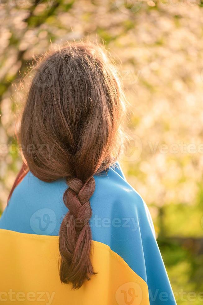 Girl with yellow and blue flag of Ukraine on a background of trees in the garden. Teenager. photo