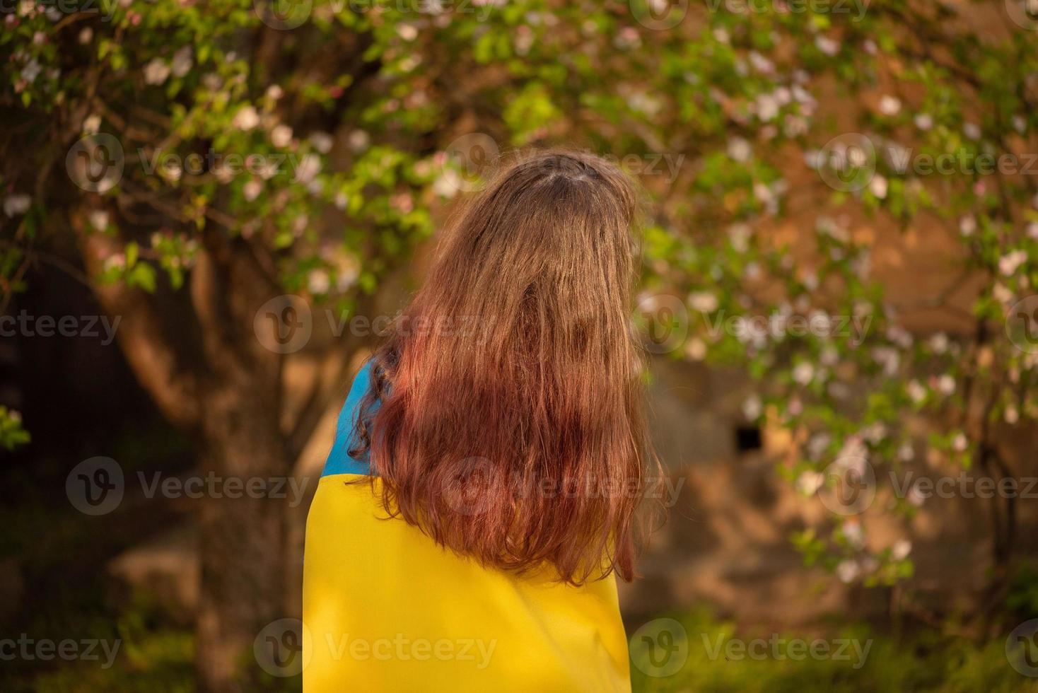 Yellow and blue fabric on the girl. Teen girl is standing with the Ukrainian flag. photo