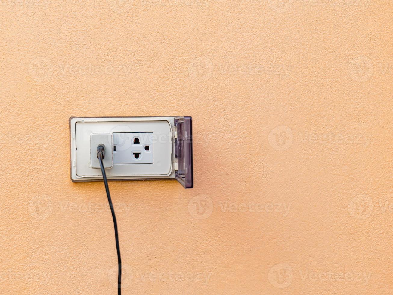 adaptador blanco viejo hay un cable de carga enchufado. con enchufes de pared para exteriores, hay una cubierta que se cierra cuando no está en uso para evitar peligros. hay un espacio de copia. foto