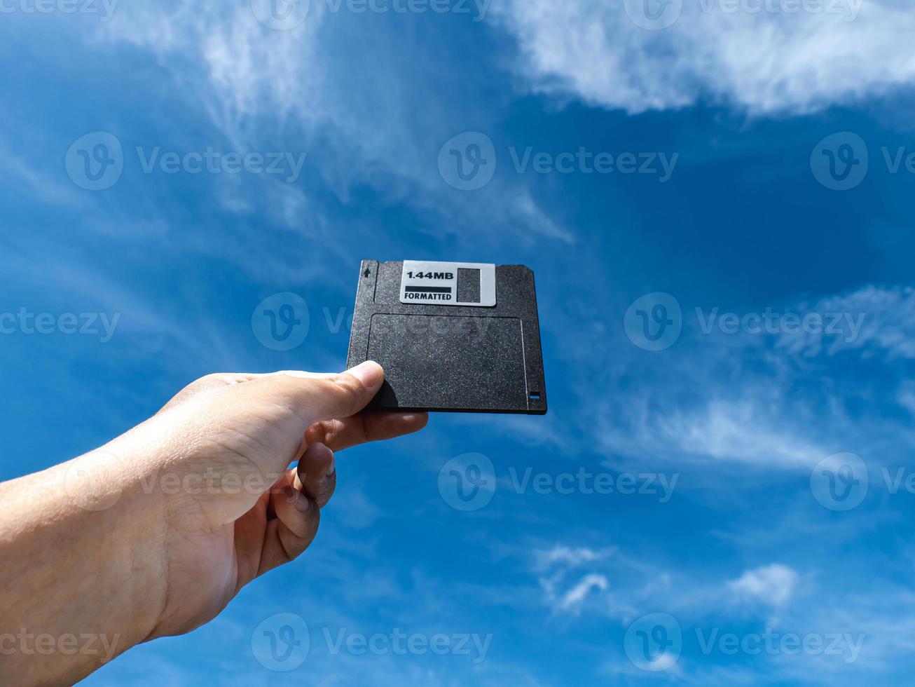 Hand holding a Floppy A disc, insert the reader. to read and write data It's technology old that have been used for a long time has a square shape the background is the sky photo