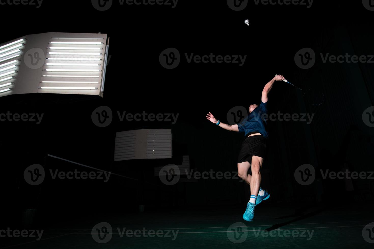 jugador profesional de bádminton usa raqueta golpeó la lanzadera o la lanzadera en la cancha durante el juego de calentamiento antes de la competencia del torneo en un solo hombre en la cancha cubierta foto