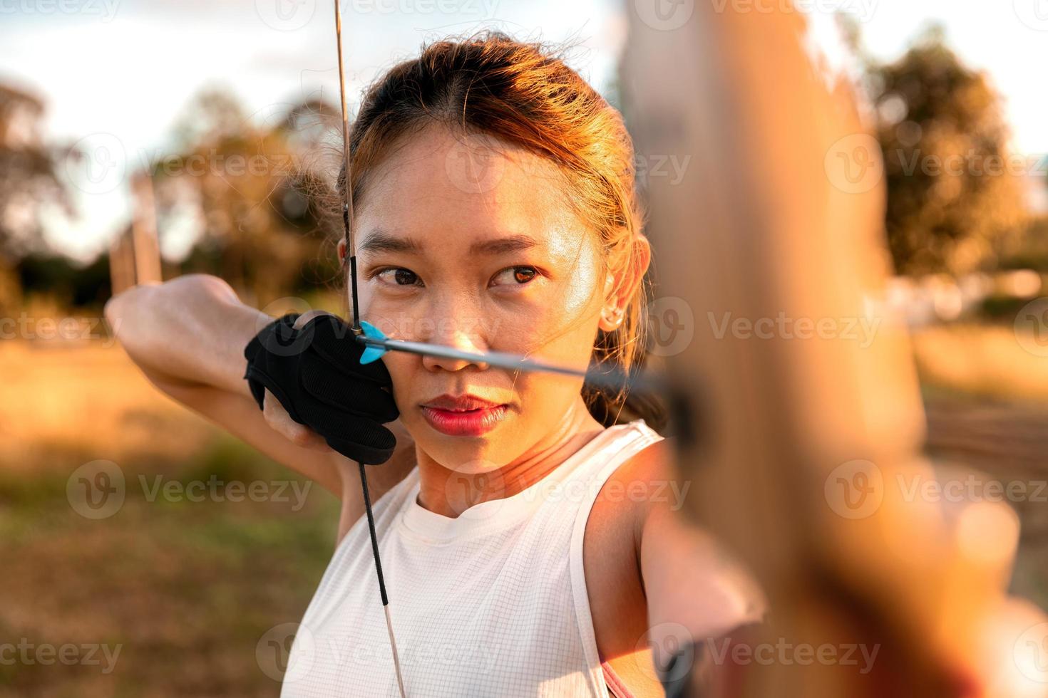 joven arquera, tiro con arco, disparar con arco en el campo natural al objetivo, concepto de éxito, en el campo para el ejercicio deportivo al atardecer foto