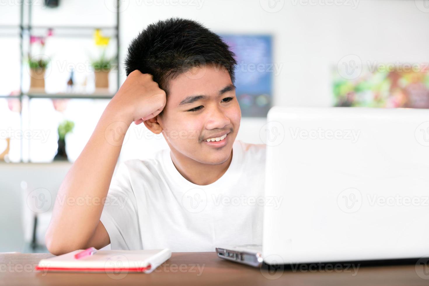 un estudiante asiático feliz usa auriculares y estudia en línea con una videollamada enseñada por un maestro con una tableta inteligente y una computadora portátil desde casa durante el covid-19 foto