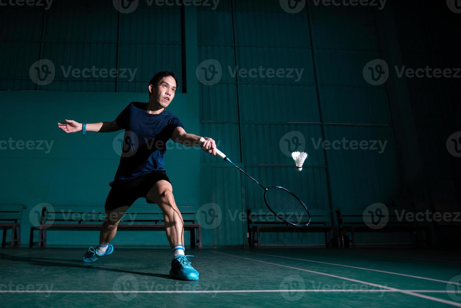 jugador profesional de bádminton usa raqueta golpeó la lanzadera o la lanzadera en la cancha durante el juego de calentamiento antes de la competencia del torneo en un solo hombre en la cancha cubierta foto