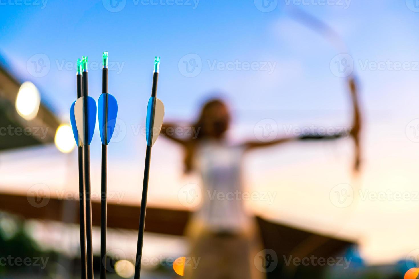 young female archer, archery, shoot arow with bow in nature field to target, success concept, at field for sport exercise at sunset time photo