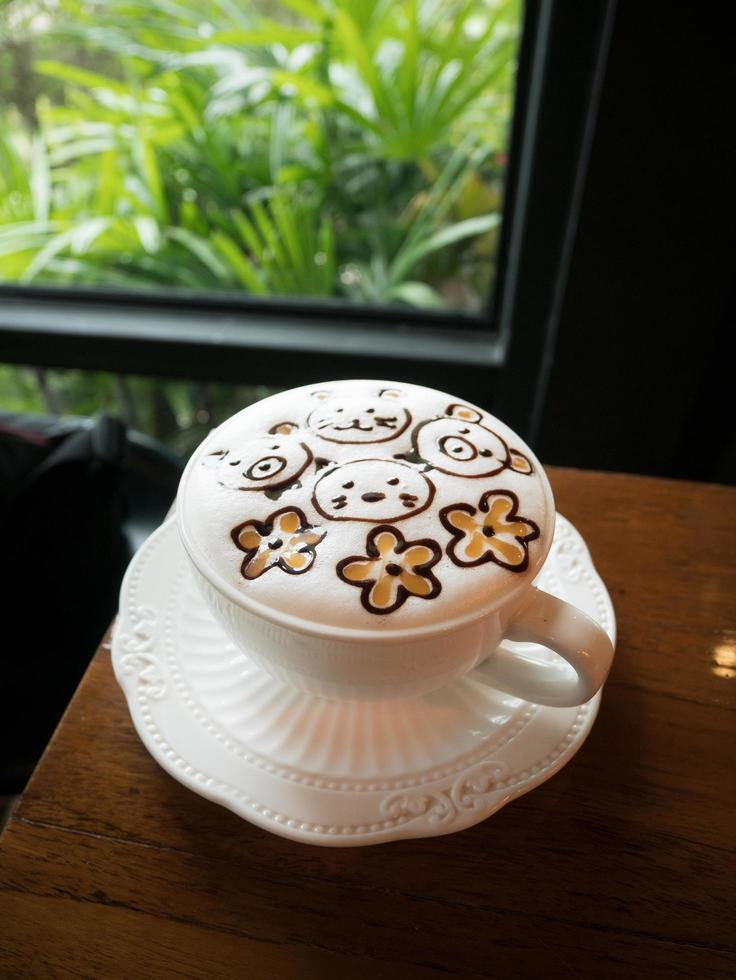Cappuccino with fresh milk foam and latte art in a white ceramic glass on a wooden table at a coffee shop. photo