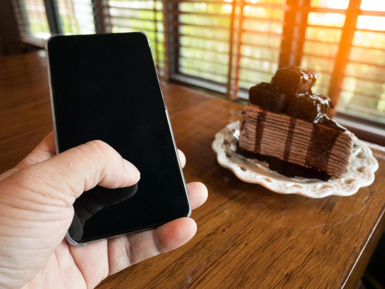 Chocolate cake with young businessman hand holding phone with blank screen For advertising, enter a message or promotion topic at the coffee shop. photo