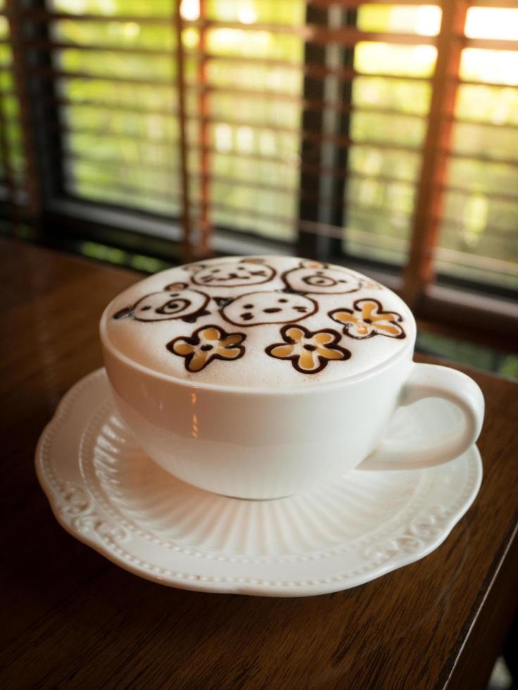 Cappuccino with fresh milk foam and latte art in a white ceramic glass on a wooden table at a coffee shop. photo