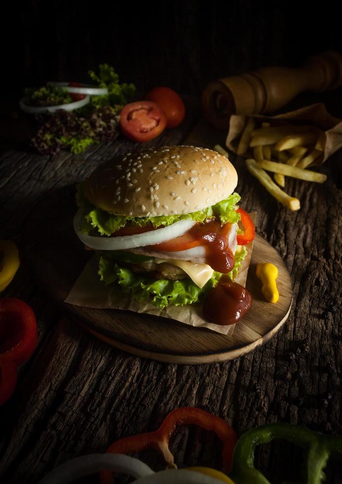 Pork hamburger Homemade with grilled bacon contains vegetables, cheese, lettuce, onion, chilli, spices in a wooden dish on a wooden floor. photo