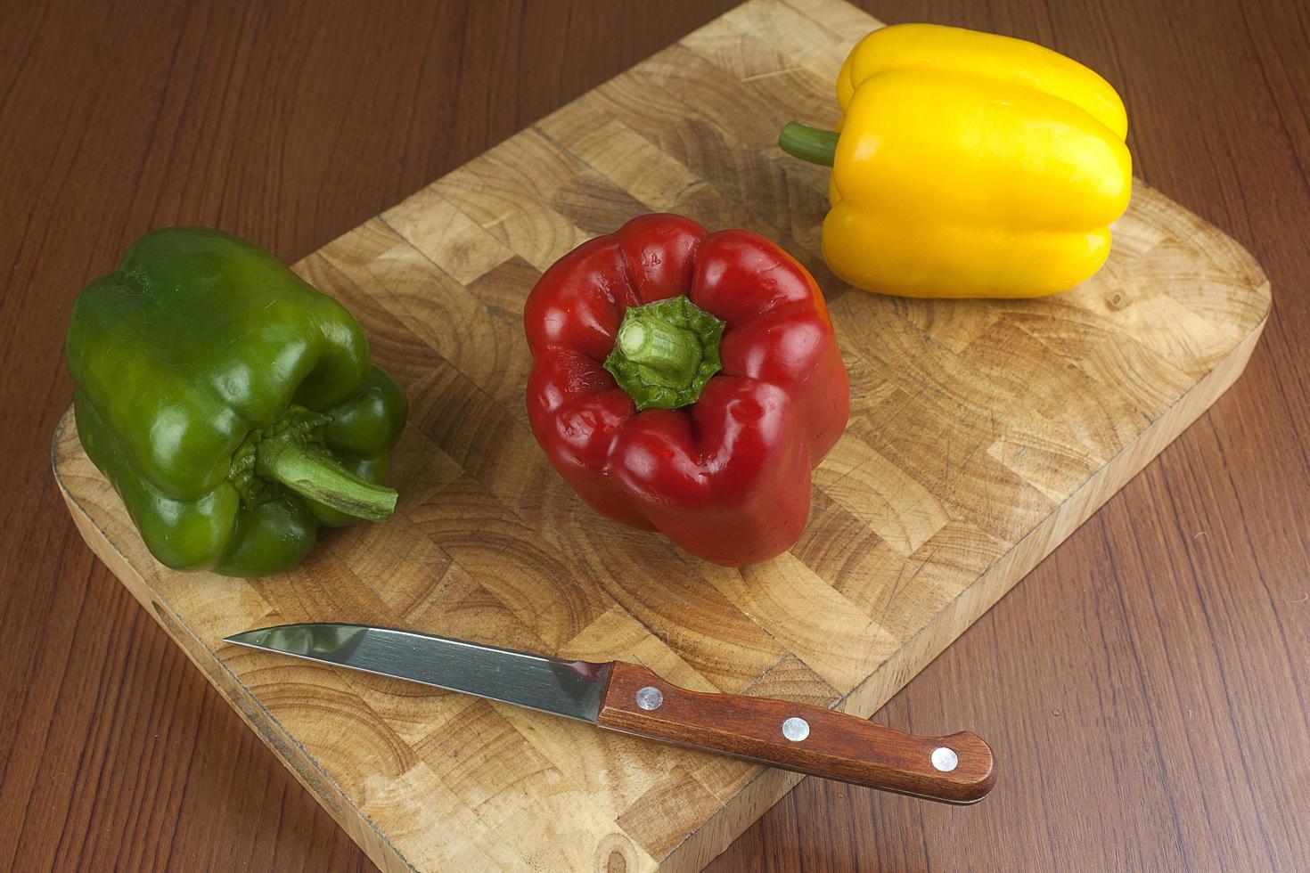 tres pimientos picantes en una tabla de cortar de madera con un cuchillo sobre la mesa. foto