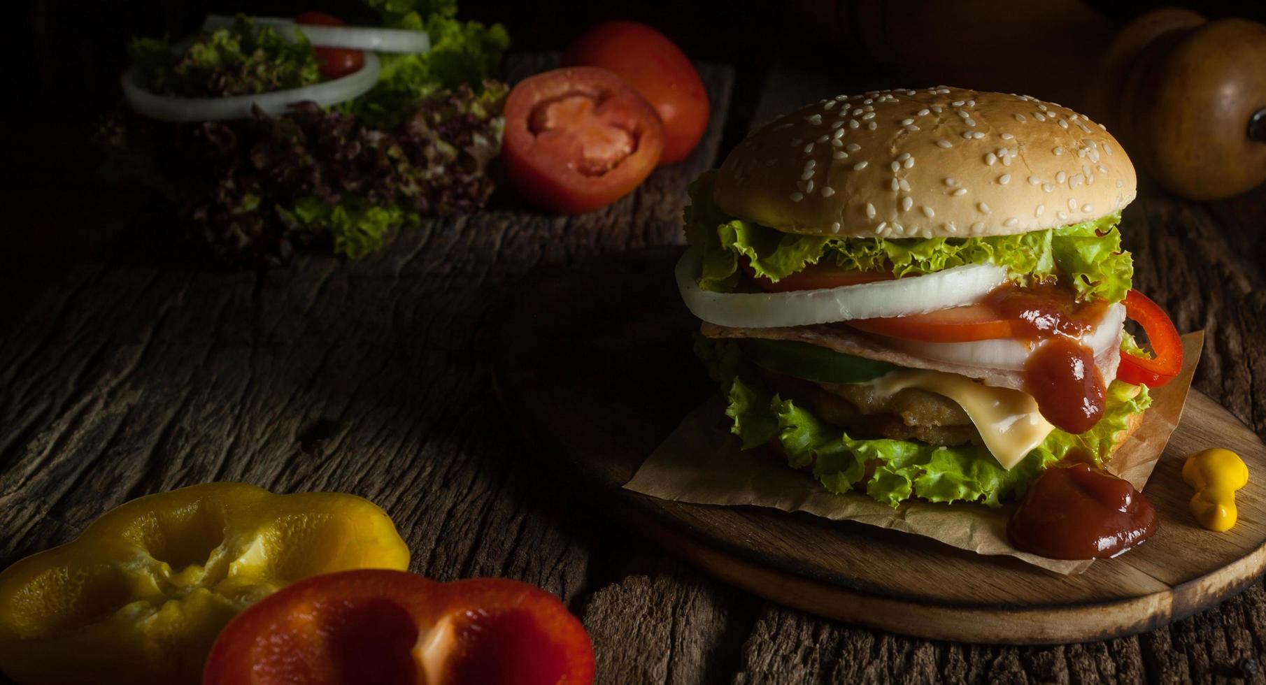 hamburguesa de cerdo casera con tocino a la parrilla contiene verduras, queso, lechuga, cebolla, chile, especias en un plato de madera sobre un suelo de madera. foto