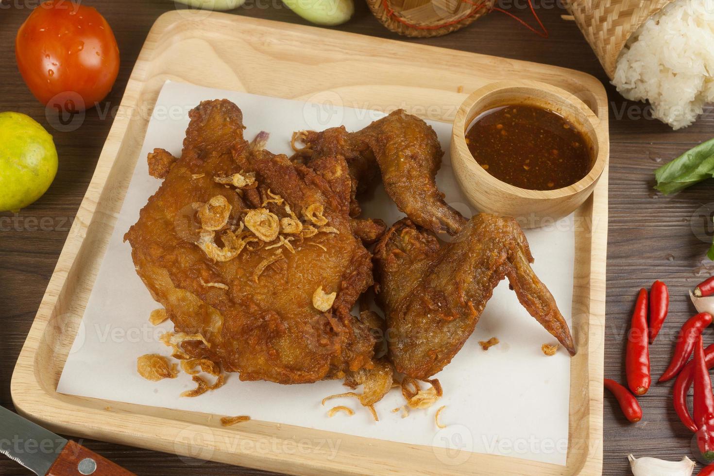 Fried chicken with spices on wooden plate with sauce and vegetables photo