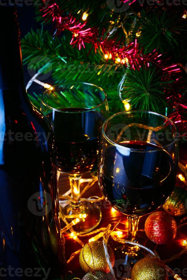 vino tinto en vidrio transparente, árbol de navidad y adorno en mesa de madera listo para celebrar. foto