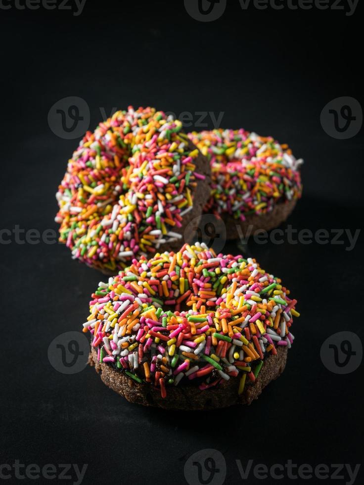 three glazed Donut with colorful sprinkles isolated on black background. angel view. photo
