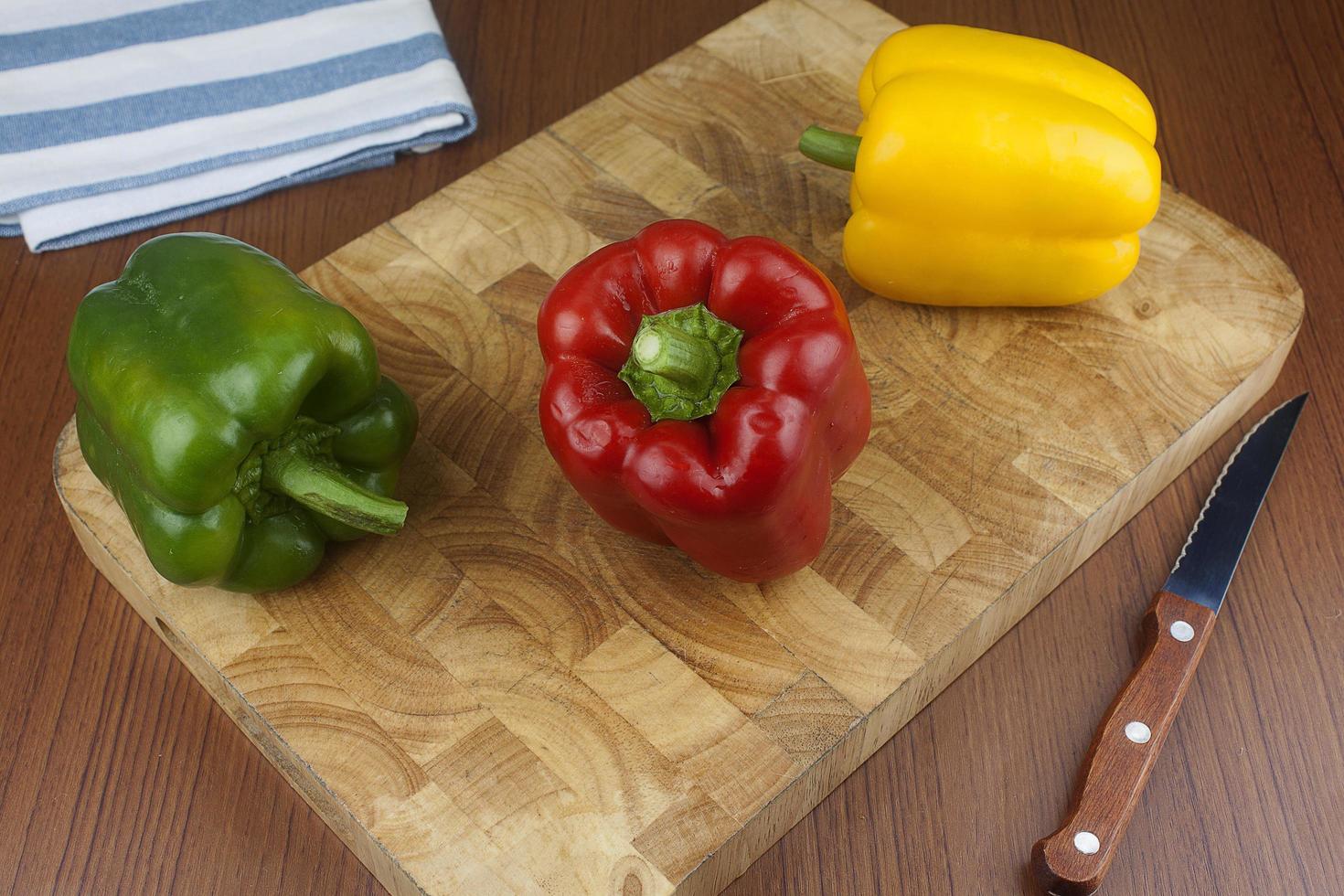 Three chili bell pepper on a wooden cutting board with knife on the table. photo