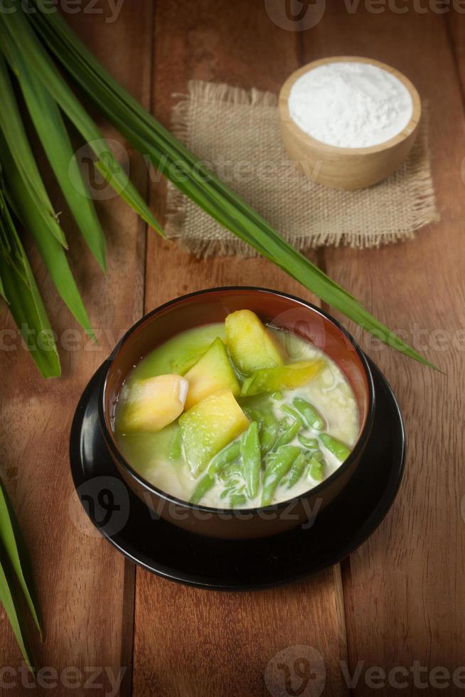 postres tailandeses hechos de harina. , leche de coco, azúcar de coco, olor a pandan al vapor hasta una línea. luego vierta con leche de coco fresca. los melones se colocan en un recipiente negro. poner en piso de madera, lot chong foto