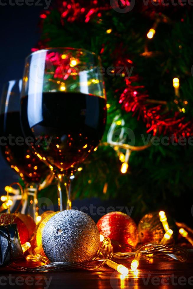 vino tinto en vidrio transparente, árbol de navidad y adorno en mesa de madera listo para celebrar. foto