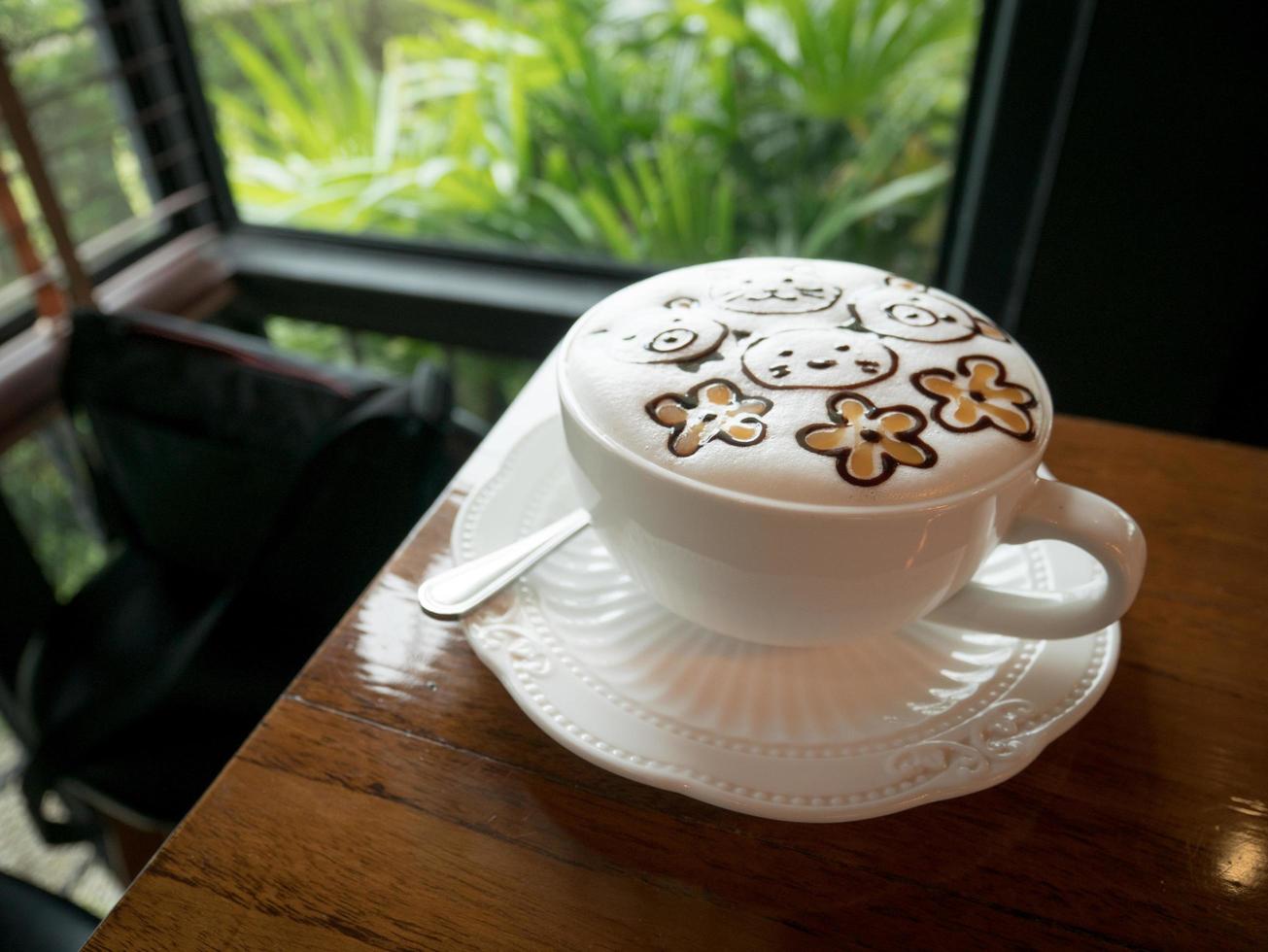 Cappuccino with fresh milk foam and latte art in a white ceramic glass on a wooden table at a coffee shop. photo